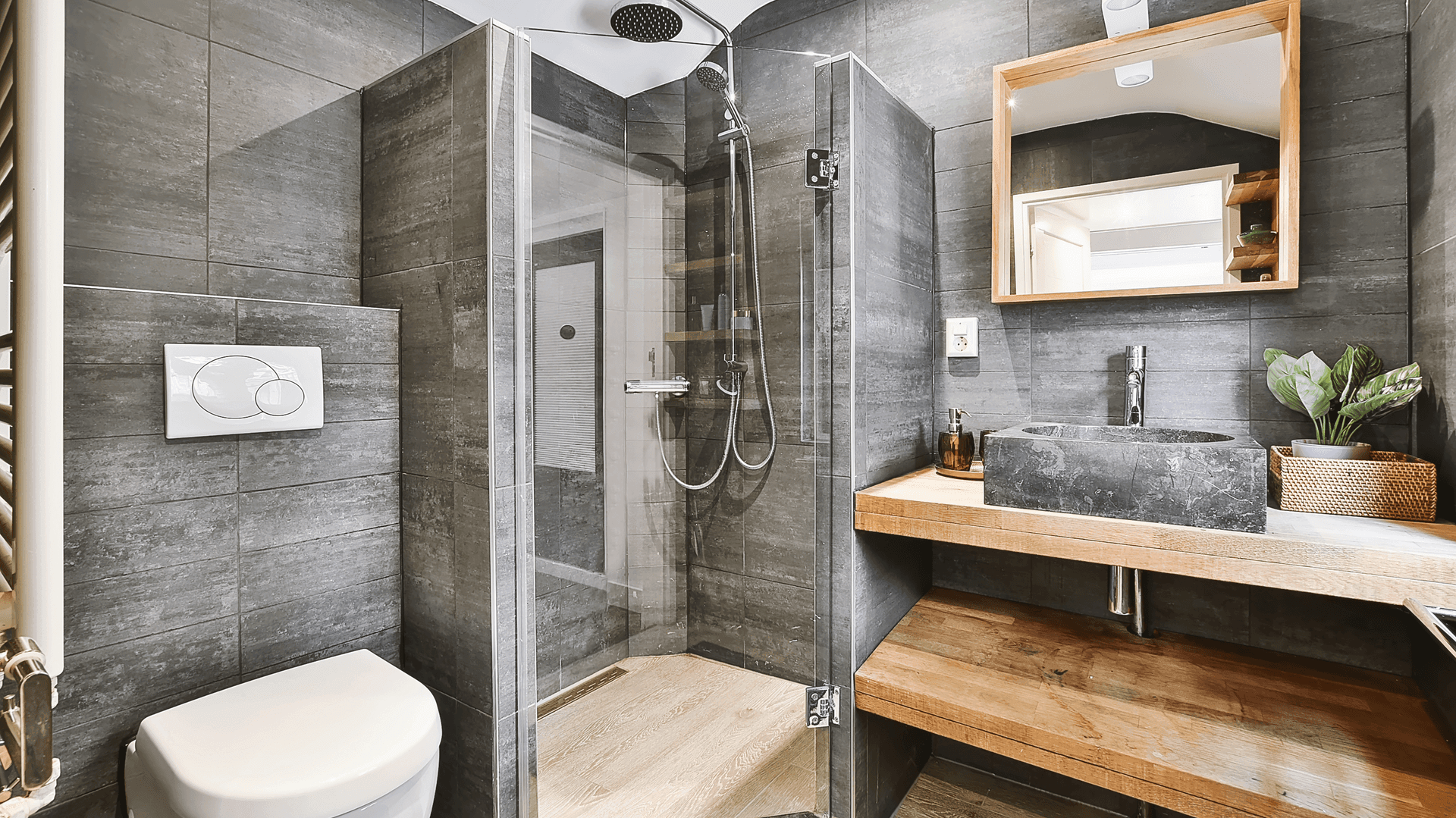 Modern bathroom with glass shower, dark tiles, stone sink, and wood accents.